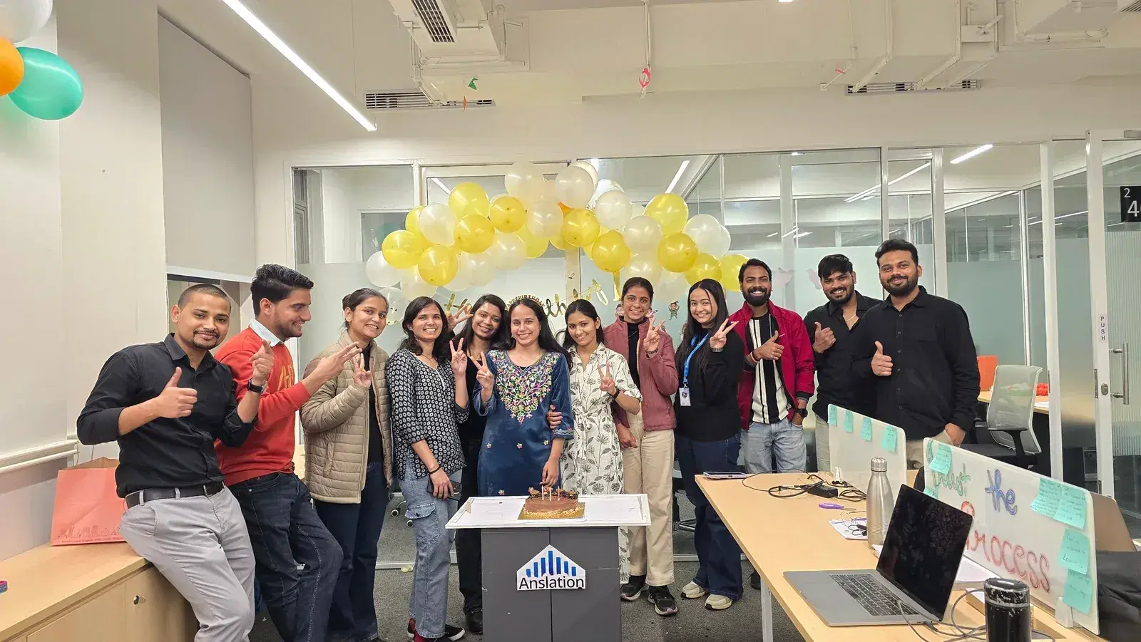 The ANSI team gathered around a birthday cake under a balloon arch